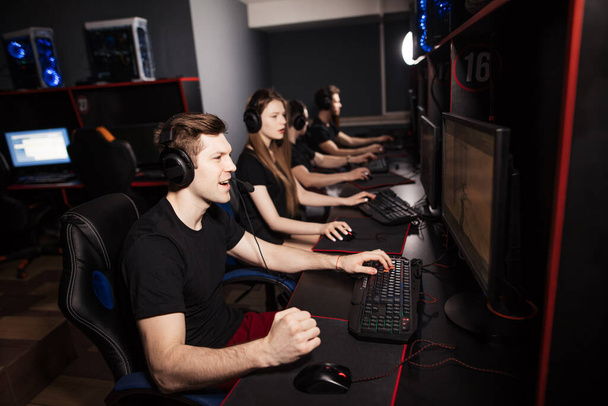 Group of adult gamers sit in row behind the monitors play in PC gaming centre. - Foto, Imagem