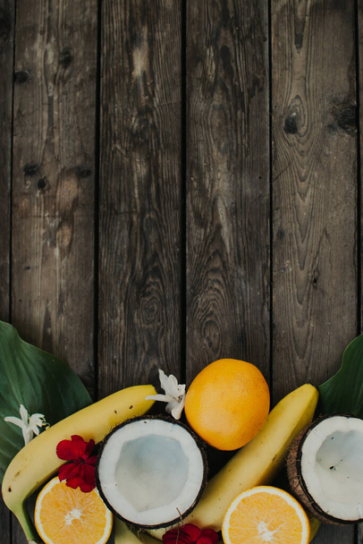 Frutos tropicales sobre fondo de madera. Fondo de frutas. Coco, naranjas y plátanos sobre una mesa de madera. - Foto, Imagen