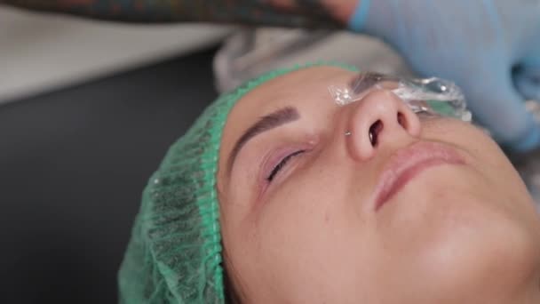 Un maquillador permanente se hace un tatuaje en los párpados superiores de una mujer. - Metraje, vídeo