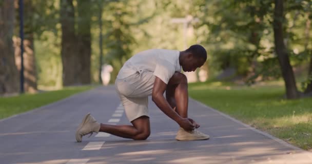 Schwarzer Sportler bindet Schnürsenkel auf Laufstrecke - Filmmaterial, Video