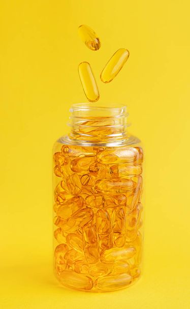 Cápsulas de aceite de pescado cayendo en el frasco sobre fondo amarillo. Suplemento nutricional - Foto, Imagen