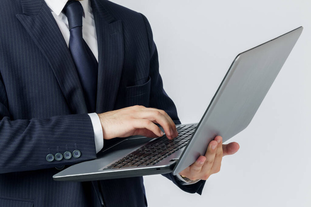 A businessman is holding a laptop in his hands, is typing with one hand. White background. No face visible. Business and finance concept - Photo, Image