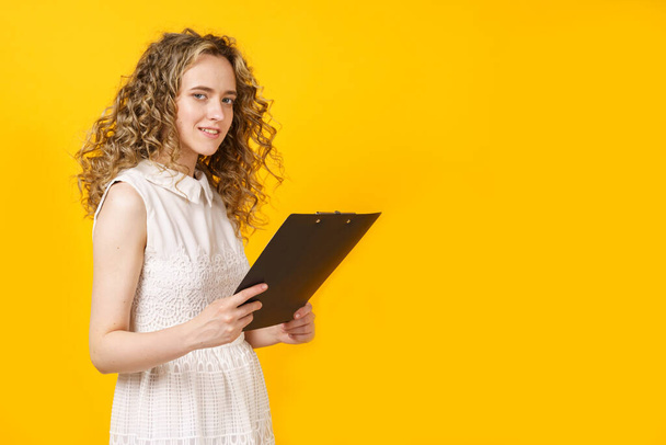 Portrait of a young woman who holds a tablet in her hands. Female portrait. Isolated on yellow background - Фото, зображення