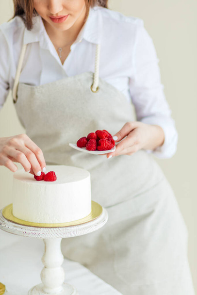 young pleasant woman putting berries on the top of the cake - Foto, Imagem