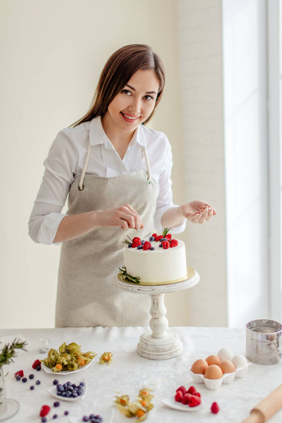 cheerful pretty girl putting berries on the top of the cake - Photo, Image