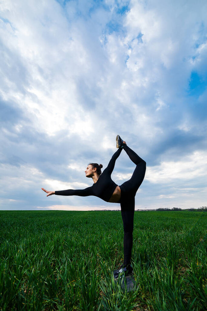 Schöne Turnerinnen auf dem grünen Rasen machen Yoga. Eine schöne junge Frau auf einem grünen Rasen führt akrobatische Elemente vor. Flexible Turnerin in Schwarz macht Handstand im Split - Foto, Bild