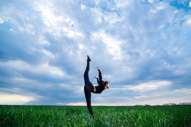 Yeşil çimenlerin üzerinde güzel bir kız model yoga yapıyor. Yeşil çimenlikte güzel bir esmer akrobatik elementler sergiliyor. Esnek siyahlı jimnastikçi egzersiz yapıyor. - Fotoğraf, Görsel