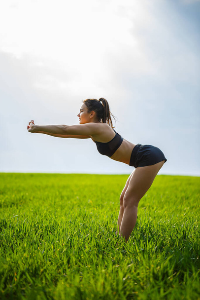 Morning workout. Healthy lifestyle concept. Young attractive woman in sportswear makes stretching her hand before training on the nature at dawn. Muscle warming - Zdjęcie, obraz