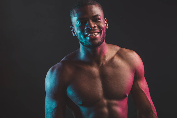 African male bodybuilder champion with naked torso posing at studio on black . - Photo, Image