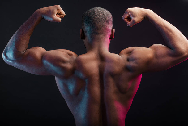 African bodybuilder in Back double biceps position, over dark background. - Foto, Imagem