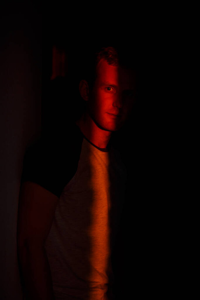Dramatik, zarif, yüzünde ışık saçan genç bir adam stüdyodaki kameraya bakıyor. - Fotoğraf, Görsel
