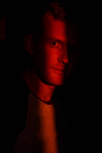 драматичный элегантный молодой человек с лучом света на лице смотрит в камеру в студии - Фото, изображение