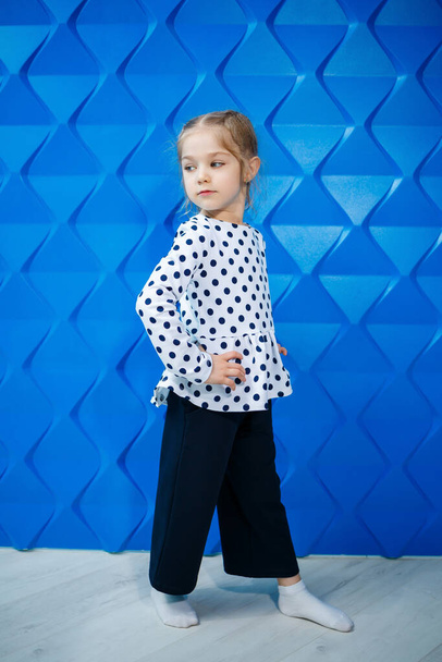 Una ragazza bionda di 7 anni in giacca con piselli su sfondo blu balla e ride, emozioni di gioia per bambini brillanti, un'infanzia felice - Foto, immagini