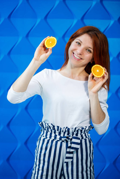 Девушка на ярко-голубом фоне в белой блузке с апельсинами в руке - Фото, изображение
