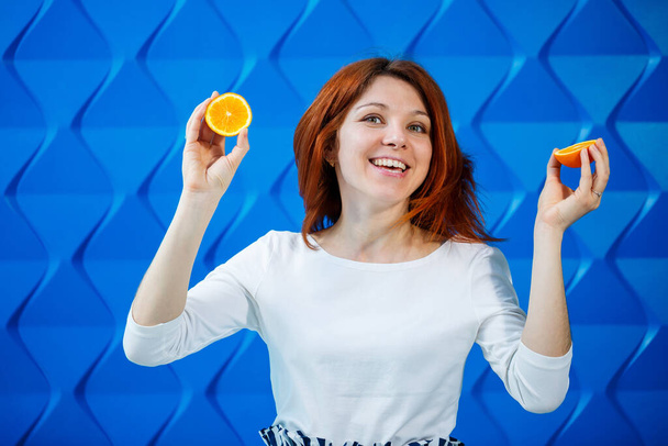 Девушка на ярко-голубом фоне в белой блузке с апельсинами в руке - Фото, изображение