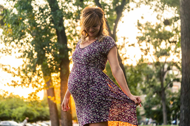 Una mujer embarazada sonriente parada en el parque de la ciudad - Foto, Imagen