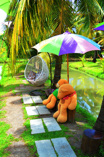 Zwei Braunbärpuppen unter buntem Regenschirm und eine Schaukel im Garten - Foto, Bild