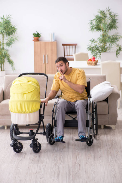 Jovem empreiteiro em cadeira de rodas cuidando de recém-nascido - Foto, Imagem