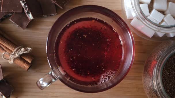 Proces vaření červeného karkádového čaje, zblízka shora. Koncept. Šálek čerstvě uvařeného ovocného čaje, nalévání horké vody z konvice do skleněného kelímku na dřevěném pozadí. - Záběry, video