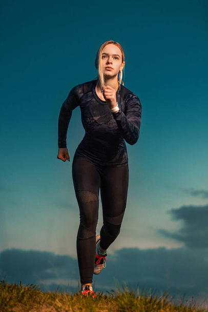 Workout outdoor. Sporty young woman and fit athlete runner running on the sky background. The concept of a healthy lifestyle and sport. Woman in black outfit. - Photo, Image