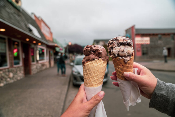 Due mani di persone tengono coni di waffle gelato in un gesto di brindisi, mentre camminano in giro. Preso nel centro di Seaside, Oregon - Foto, immagini