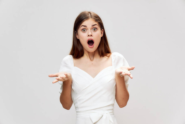 Verrast vrouw met brede open mond spreidt haar handen in een witte jurk studio  - Foto, afbeelding