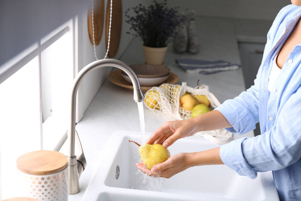 Woman washing fresh ripe pear in kitchen, closeup - 写真・画像
