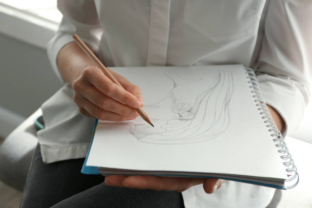 Woman drawing girl's portrait with pencil in notepad, closeup - Fotó, kép