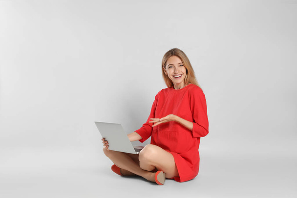 Νεαρή γυναίκα με φορητό υπολογιστή σε ανοιχτό γκρι φόντο - Φωτογραφία, εικόνα