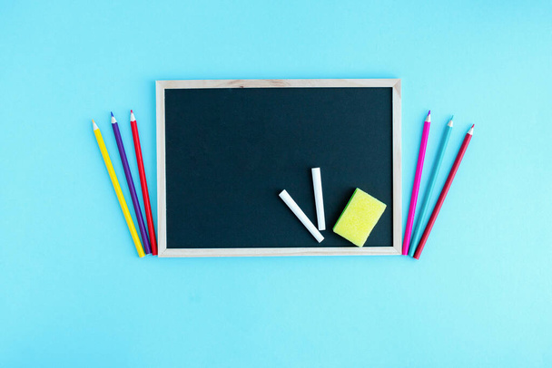 Graphite school board with a piece of chalk, a sponge and a medical protective mask on a blue background. Copy space. The beginning of the new school year. Virus protection in educational institution - Photo, Image