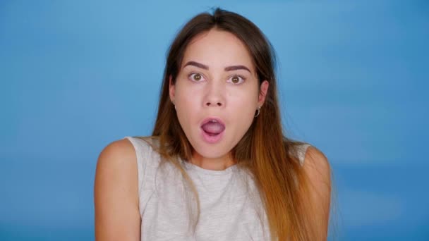 Shocked woman turns to camera on blue background with copy space - Footage, Video