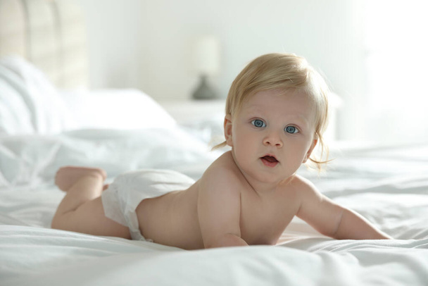 Cute little baby in diaper lying on bed at home - Foto, afbeelding
