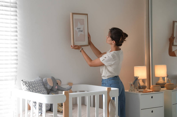 Decorator hanging picture on wall in baby room. Interior design - Φωτογραφία, εικόνα
