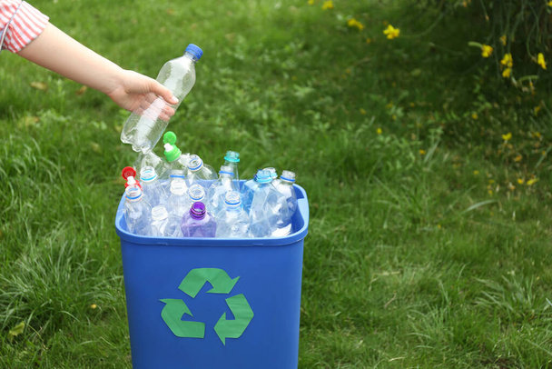 Woman throwing used bottle into trash bin outdoors, closeup. Plastic recycling - Zdjęcie, obraz