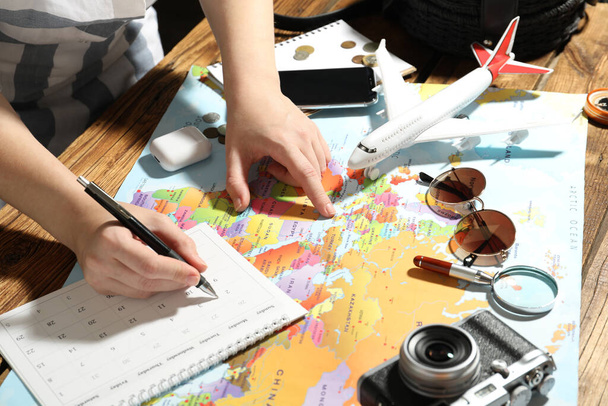Woman marking calendar at table with world map, closeup. Travel during summer vacation - 写真・画像
