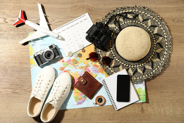 World map and items on wooden background, flat lay. Travel during summer vacation - Photo, Image
