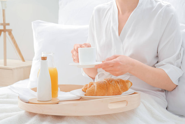Νεαρή γυναίκα τρώει πρωινό στο κρεβάτι στο δωμάτιο του ξενοδοχείου - Φωτογραφία, εικόνα