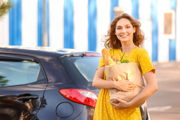 Young woman with grocery bag near car outdoors - Φωτογραφία, εικόνα