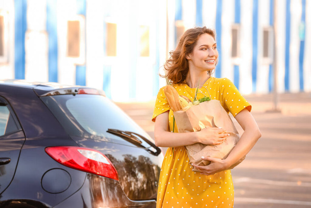 Jeune femme avec sac d'épicerie près de la voiture à l'extérieur - Photo, image