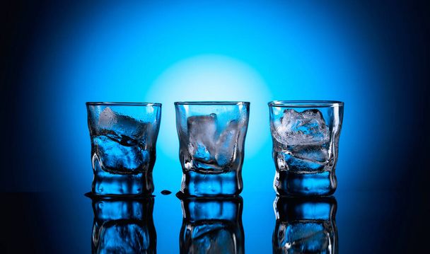 Bebida alcoólica forte em copos congelados. Óculos represados com gelo em um fundo reflexivo preto
. - Foto, Imagem