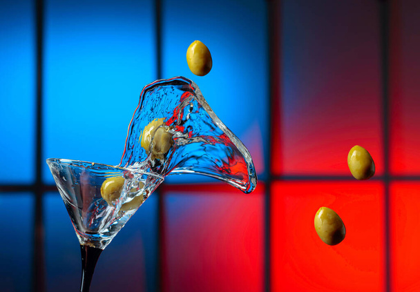 Martini y aceitunas verdes en vaso. Salpicaduras en un fondo colorido. Copiar espacio. - Foto, Imagen