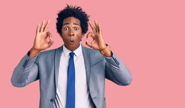 Hezký africký Američan s afro vlasy v obchodní bundě vypadá překvapeně a šokovaně dělá ok schvalovací symbol s prsty. šílený výraz  - Fotografie, Obrázek