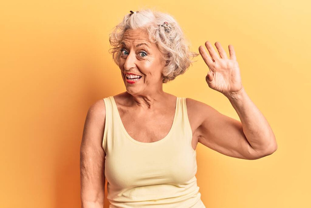 Ältere grauhaarige Frau in lässiger Kleidung verzichtet auf ein fröhliches Hallo und lächelt, freundliche Willkommensgeste  - Foto, Bild