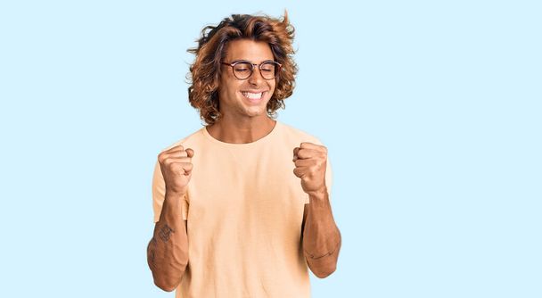 Fiatal spanyol férfi visel alkalmi ruhák és szemüveg nagyon boldog és izgatott csinál győztes gesztus felemelt karokkal, mosolygós és sikoltozó siker. ünnepség koncepciója.  - Fotó, kép