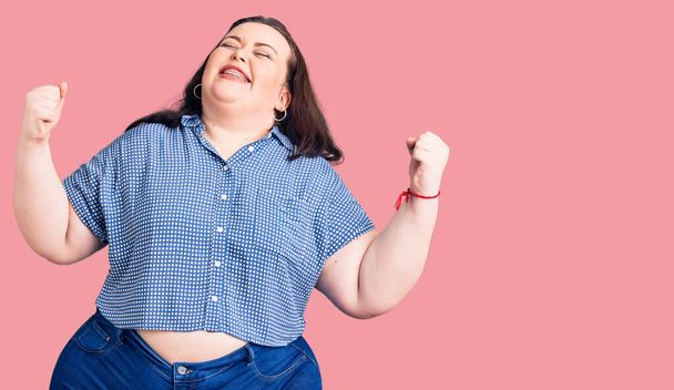 Young plus size woman wearing casual clothes very happy and excited doing winner gesture with arms raised, smiling and screaming for success. celebration concept.  - Fotografie, Obrázek