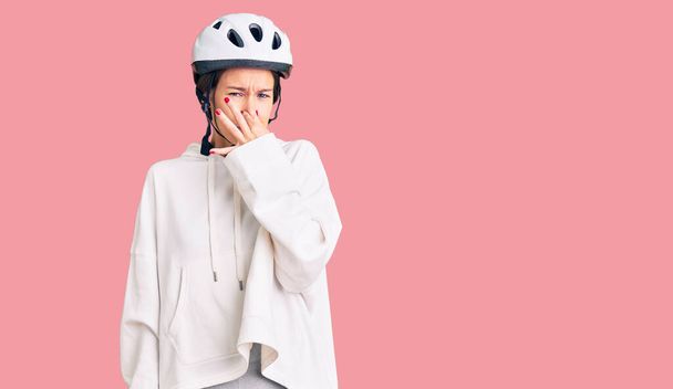 美しいブルネットの若い女性は自転車のヘルメットとスポーティな服を着て、臭いと嫌な、耐えられない匂いを嗅ぎ、鼻の上に指で息を保持する。臭いが悪い  - 写真・画像