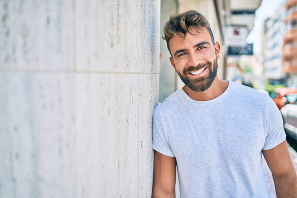 Young hispanic man smiling happy leaning on the wall at the city - Photo, Image