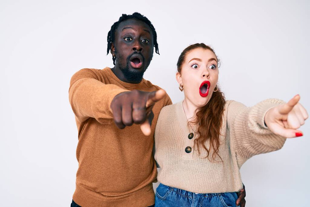 Interracial couple wearing casual clothes pointing with finger surprised ahead, open mouth amazed expression, something on the front  - Fotografie, Obrázek