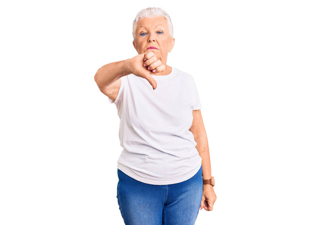 Senior beautiful woman with blue eyes and grey hair wearing casual white tshirt looking unhappy and angry showing rejection and negative with thumbs down gesture. bad expression.  - Valokuva, kuva