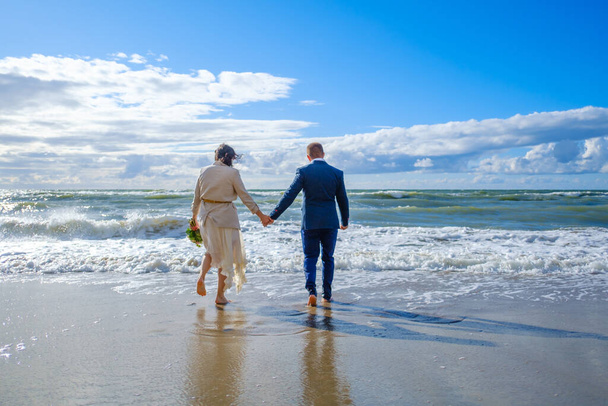 認識できない花嫁と新郎が海に向かって歩く - 写真・画像